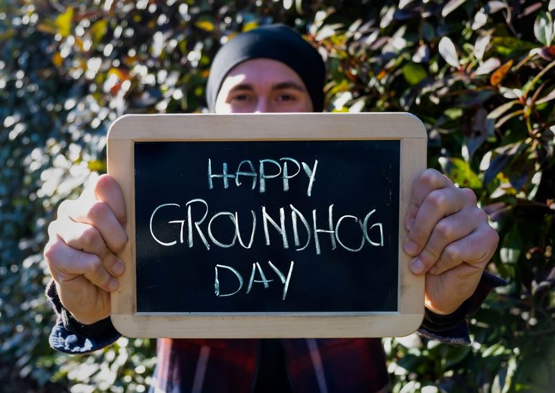 man holding a chalkboard with Happy Groundhog Day written on it