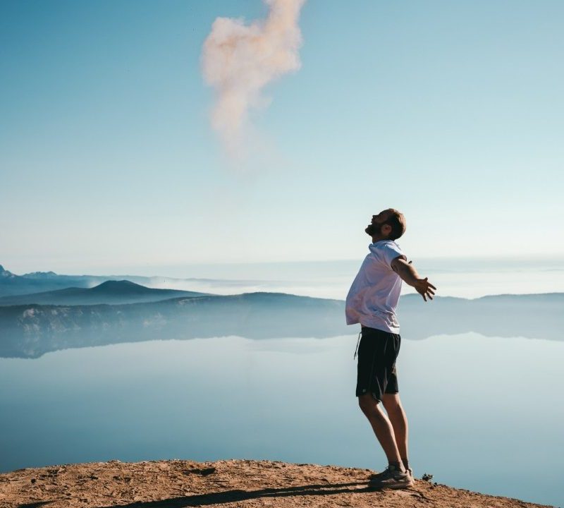 A man standing on a cliff and yelling up at the sky.