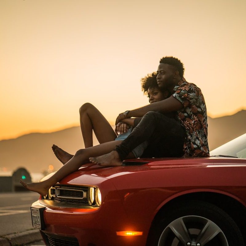 A couple relaxing in each other's arms while sitting on top of a car.