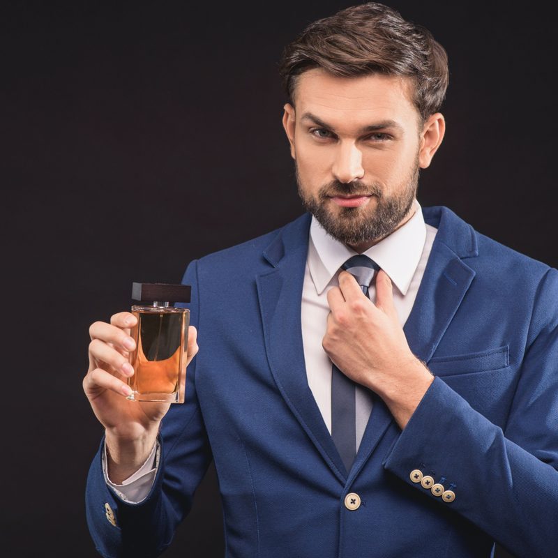 A man in a suit holding a bottle of cologne