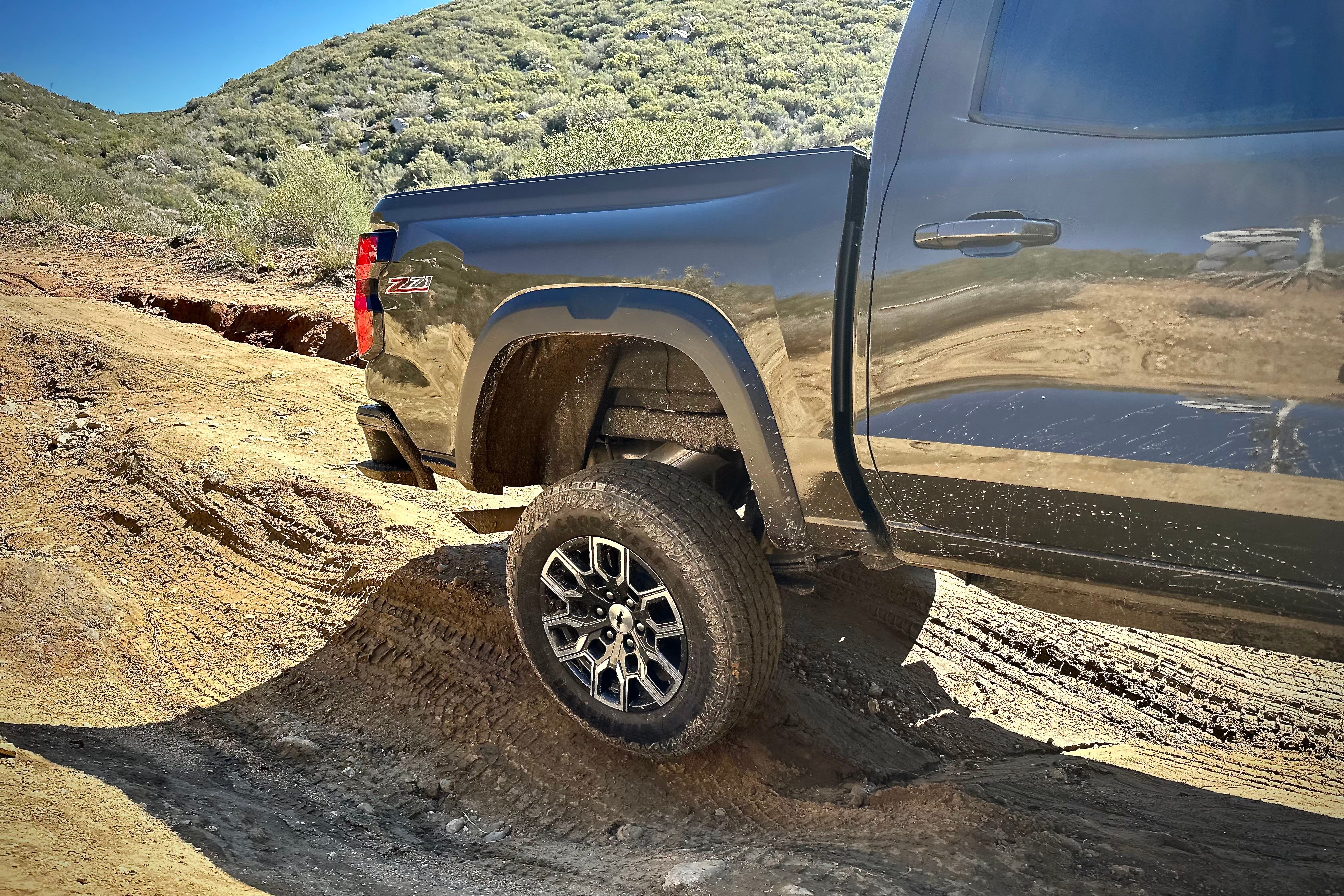 2023 Chevrolet Colorado Trail Boss off-roading close up with there rear wheel in the air with mountains in the back.