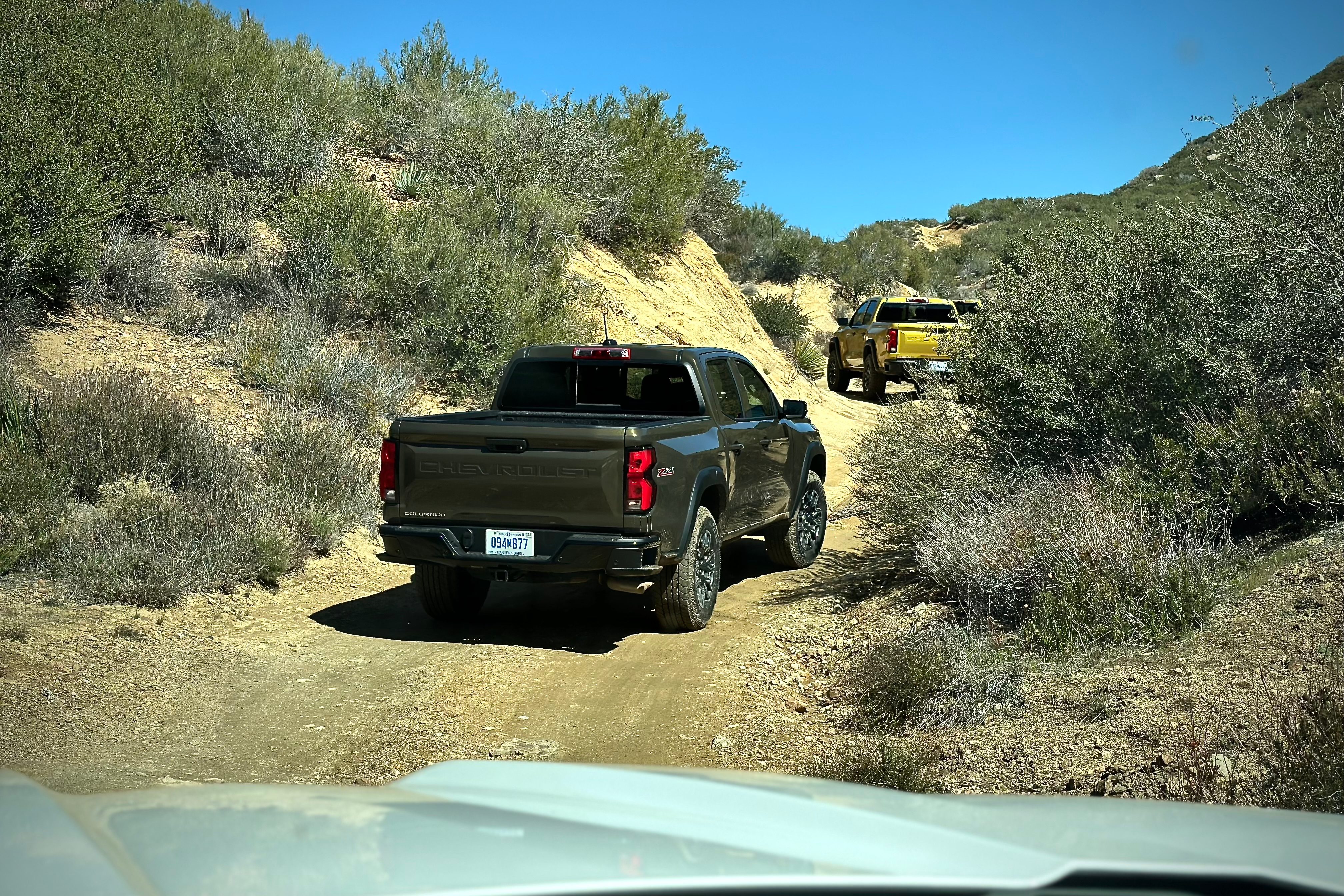 2023 Chevrolet Colorado Trail Boss off-roading on a dirt trail with mountains and bushes in the back.