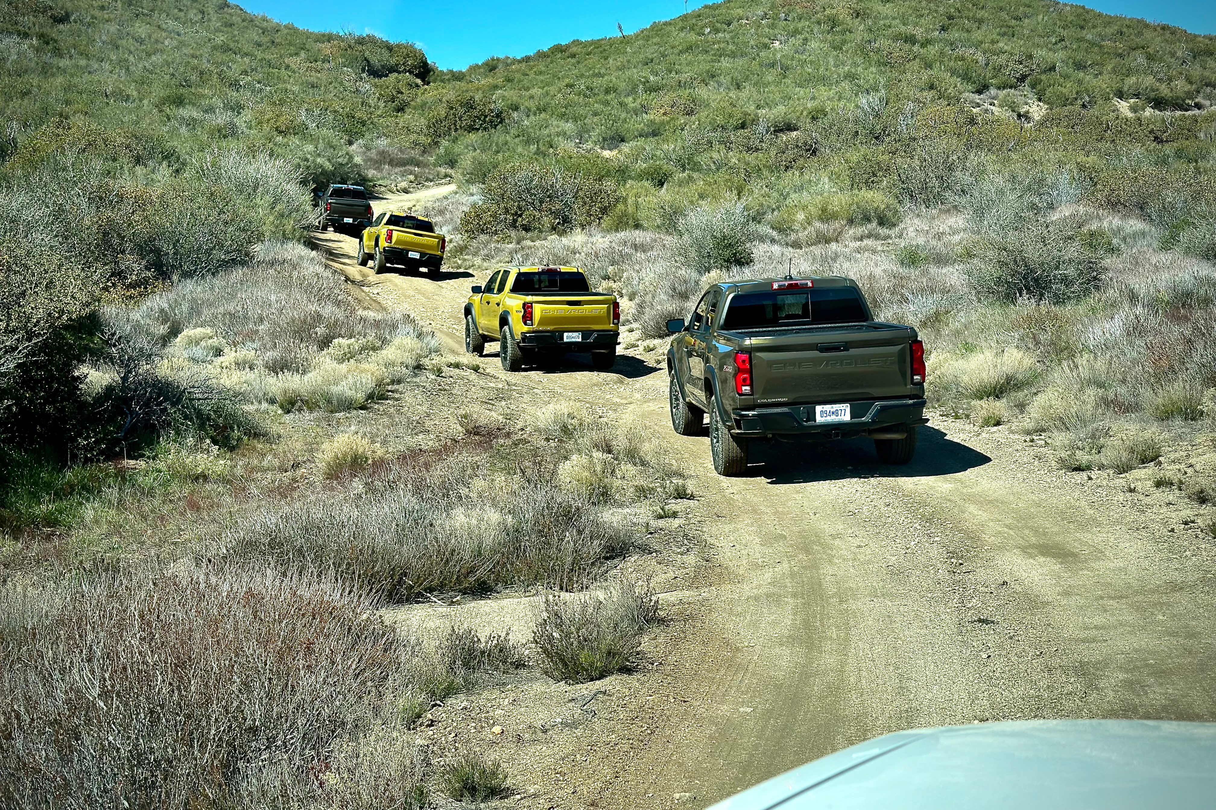 2023 Chevrolet Colorado Trail Boss off-roading on a dirt trail with mountains and bushes in the back.
