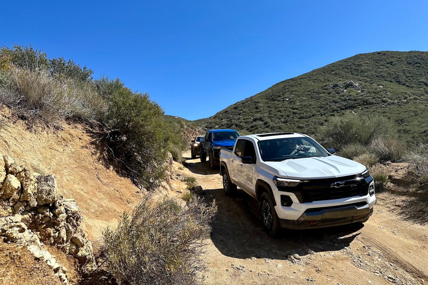2023 Chevrolet Colorado Z71 front end angle off-roading on a dirt trail with mountains in the back.