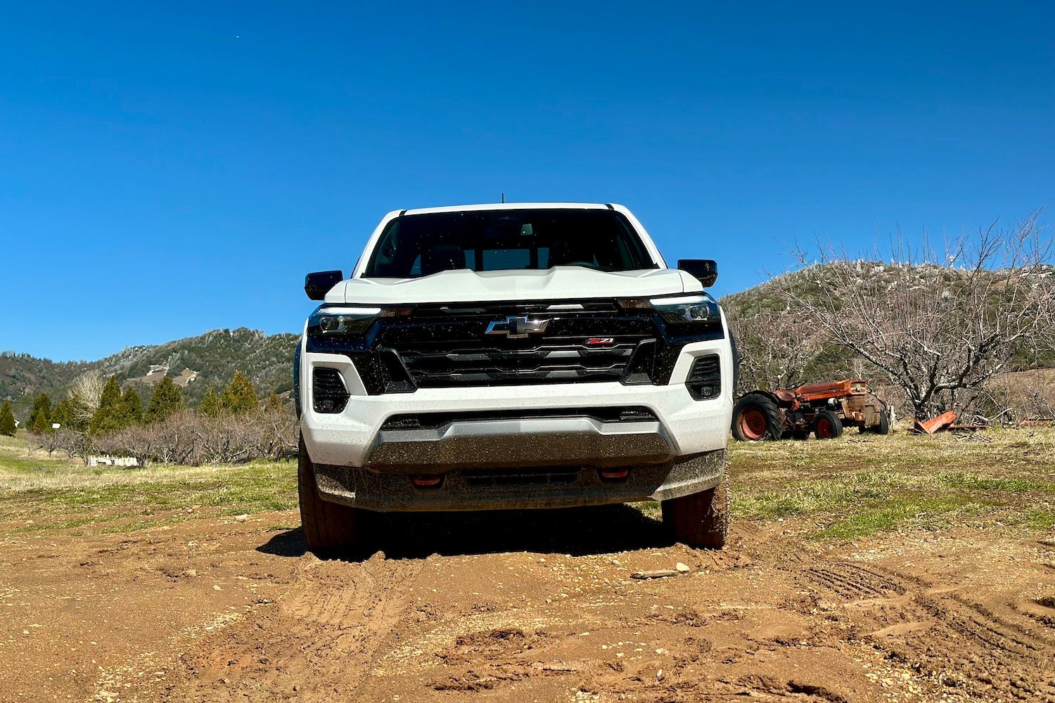 Front end close up of the 2023 Chevrolet Colorado Z71 parked in a muddy field with mountains in the back.