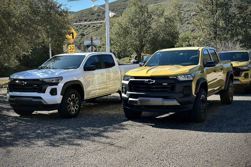2023 Chevrolet Colorado Z71 and Trail Boss parked on the side of the road with trees and mountains in the back.