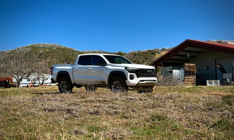 2023 Chevrolet Colorado Z71 front end angle from passenger's side parked on a grassy field in front of mountains.