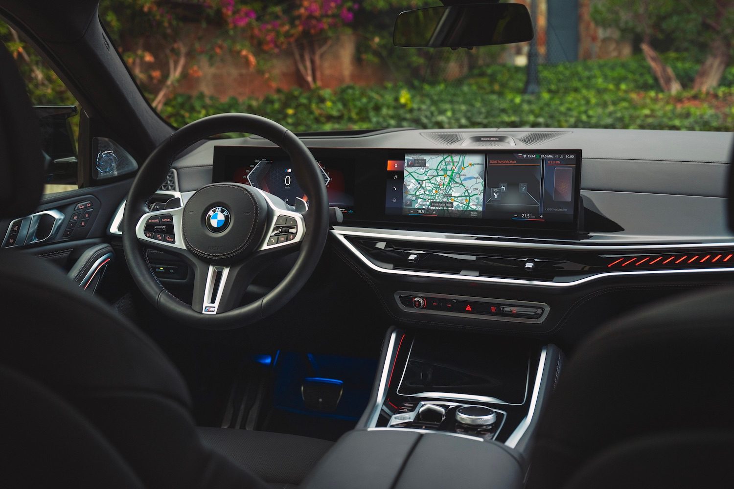 Close up of the steering wheel and dashboard in the 2024 BMW X5 and X6 from the rear seats with green grass in the back.