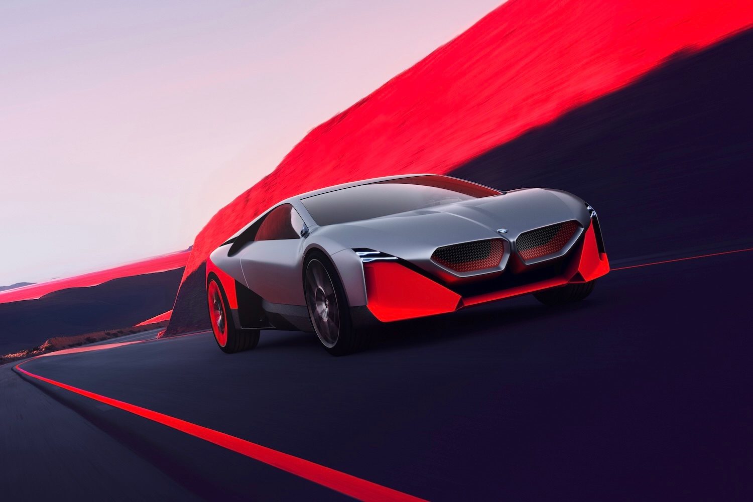 BMW M Vision NEXT Concept driving down the road from passenger's side front end angle in front of red mountains.