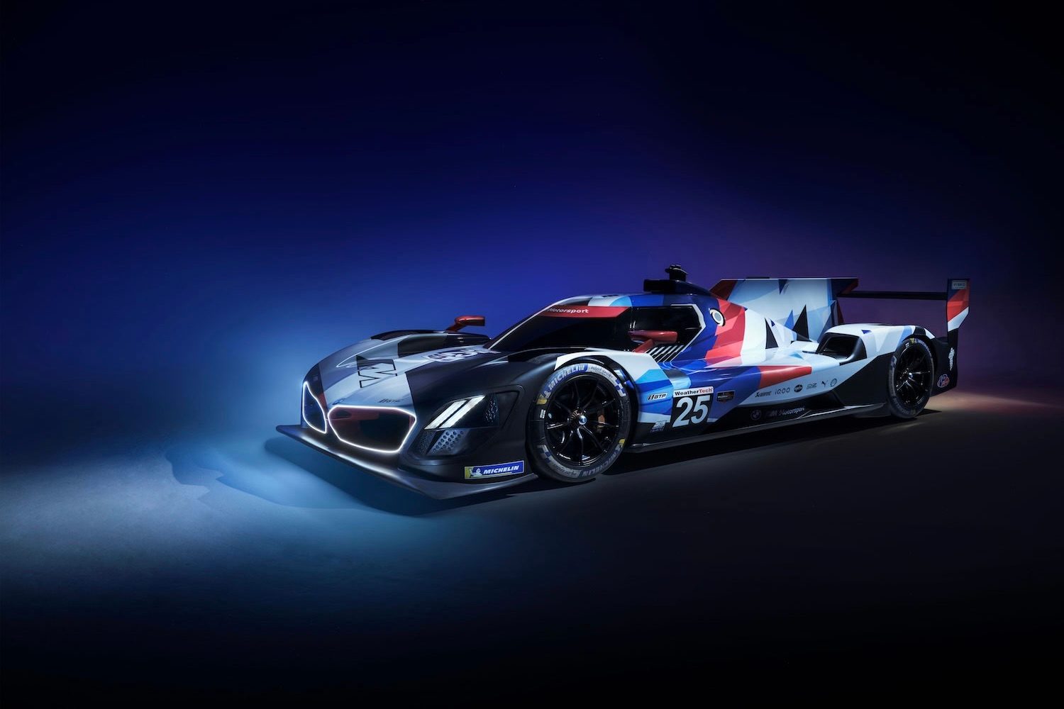 Front end angle of the BMW M8 Hybrid V8 parked in a blue studio wall with the headlights on.