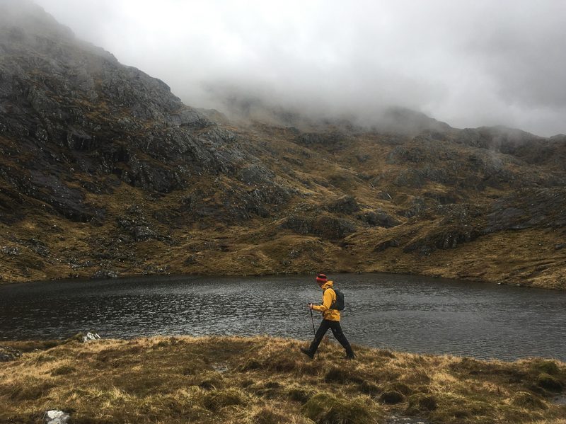 A man in a yellow GORE-TEX jacket walks past a lake
