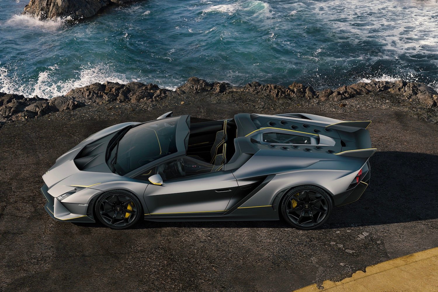 Overhead side profile of the Lamborghini Aut&eacute;ntica parked on the side of the road in front of a cliff with water.