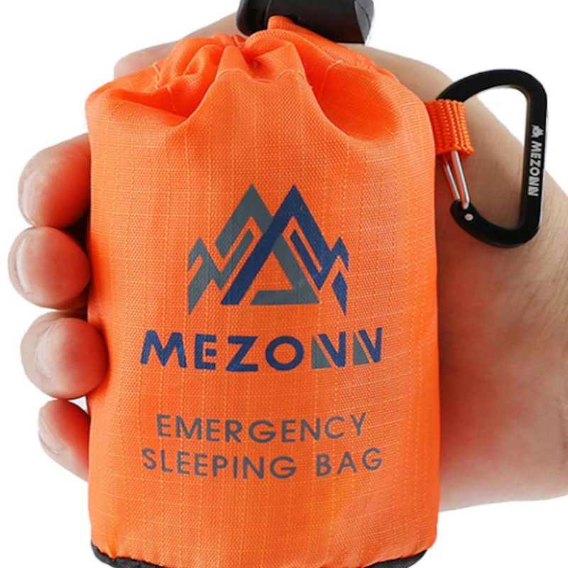 A man holding a Mezonn Emergency Sleeping Bag that's packed away in front of a white screen.