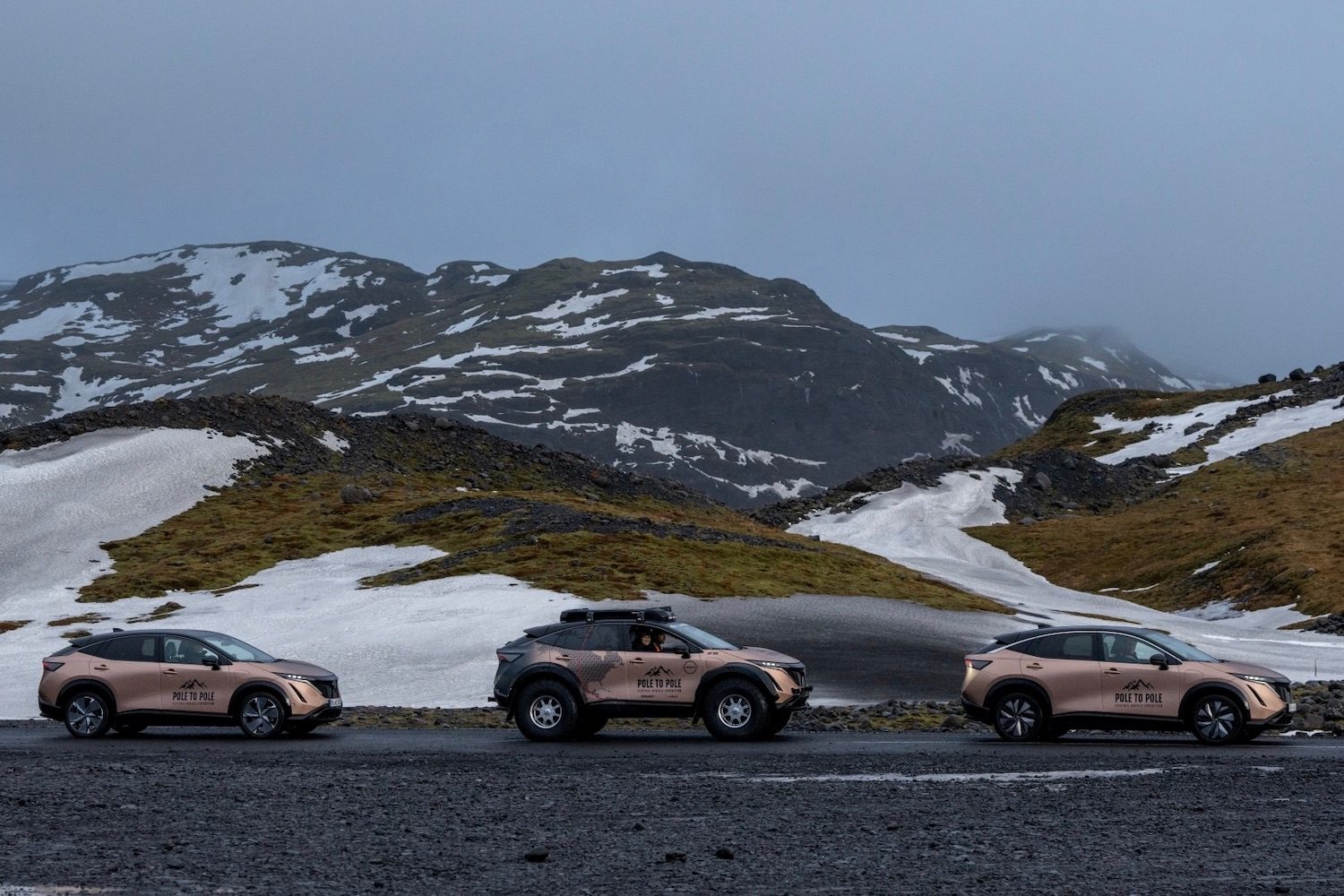Three Nissan Ariyas parked on the side of the road in front of snow-covered mountains.