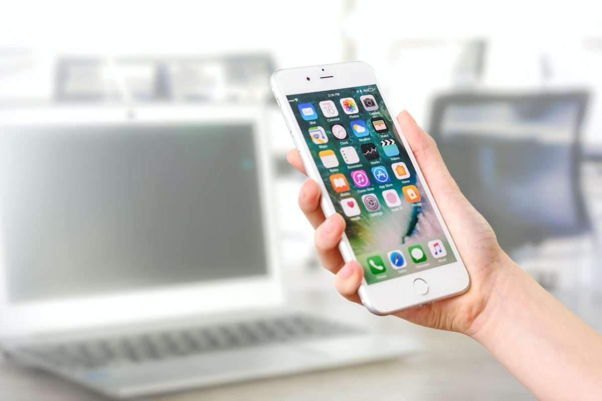 A cell phone being held in a hand in front of a laptop.