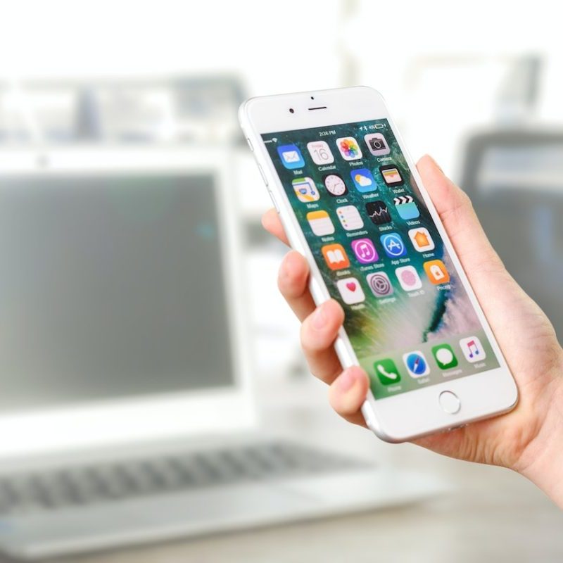 A cell phone being held in a hand in front of a laptop.