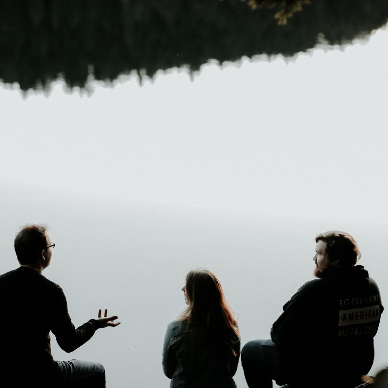 Two men and a woman sitting by a lake and talking.