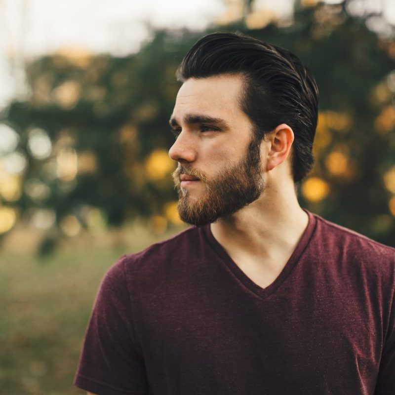 A man outside with his head to the side, wearing a beard