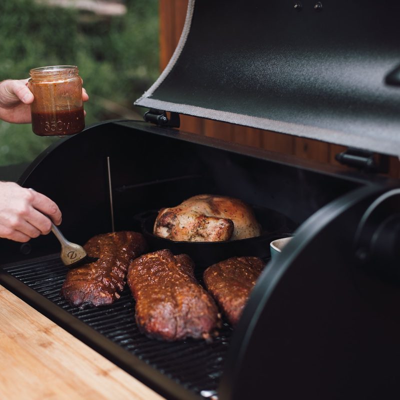 Person grilling ribs, basting with BBQ sauce