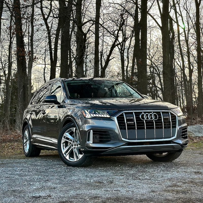 Front end angle of the 2022 Audi Q7 Prestige from the passenger's side in front of trees.