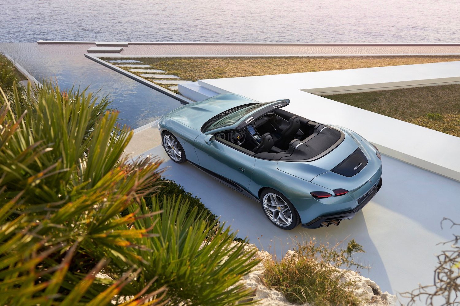 Rear overhad photo of the 2024 Ferrari Roma from driver's side parked in front of a house with water in the back.