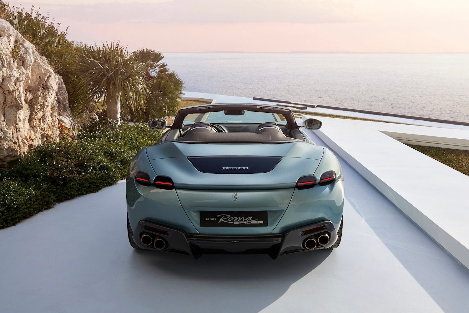 Close up of rear end of the 2024 Ferrari Roma parked in a driveway with the ocean in the back.
