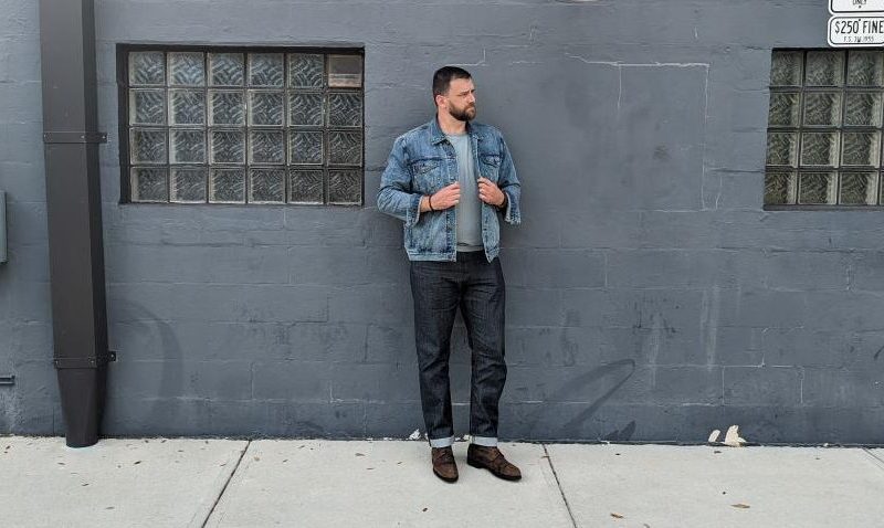 Man leaning on wall in denim jeans and jacket