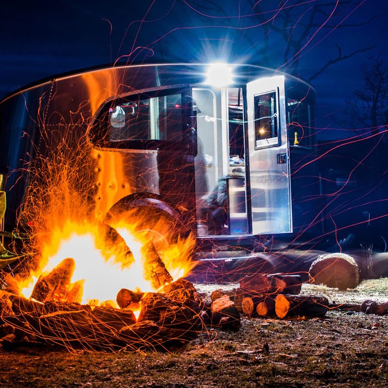 Airstream Basecamp lightweight travel trailer parked at night behind a flickering campfire.