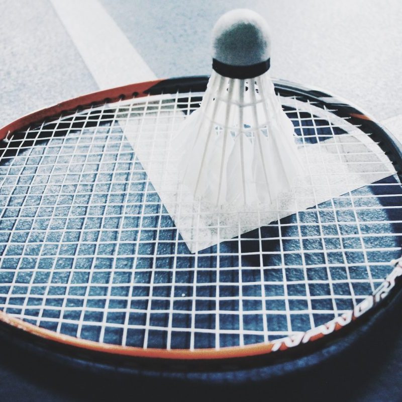 A badminton birdie on top of a badminton racket on the court floor