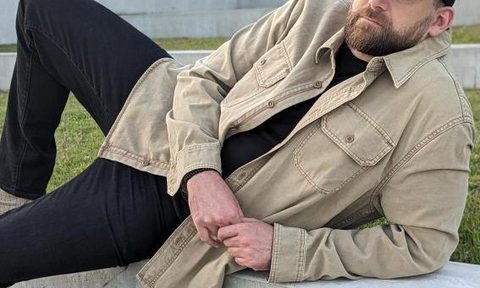 Man leaning in tan shacket and black denim