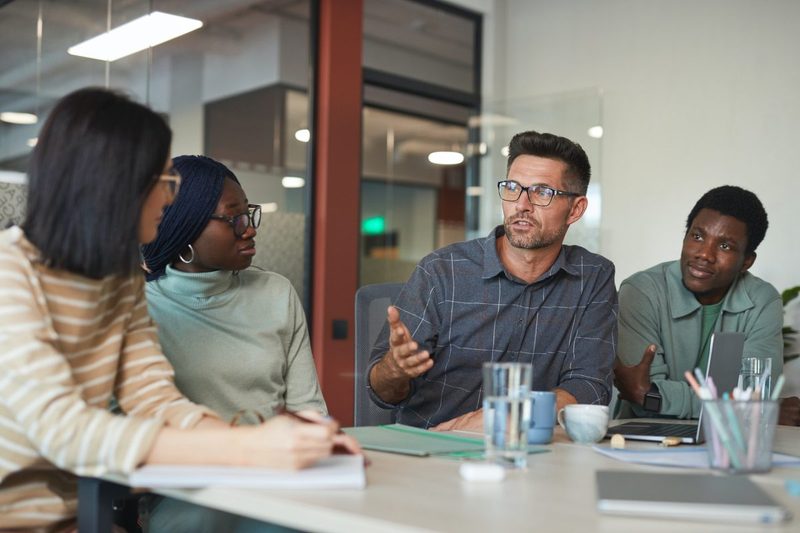People having a meeting while sitting down at a desk.