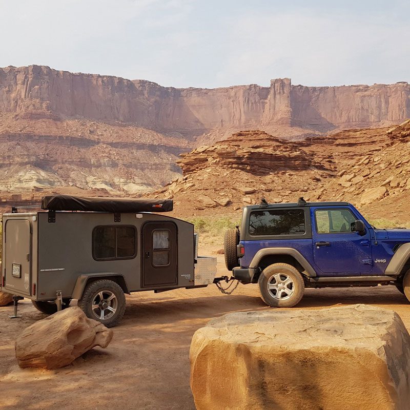 Blue Jeep towing a Hiker Trailers Mid Range Deluxe teardrop travel trailer through a mountain desert backdrop.