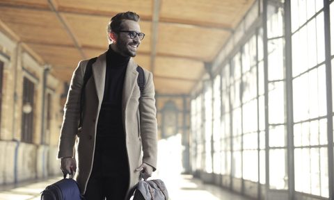 A person smilling, carrying their luggage, about to go on a trip.
