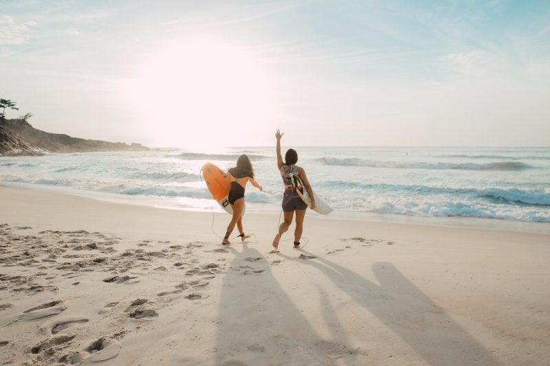 Two people about to go surfing at the beach.