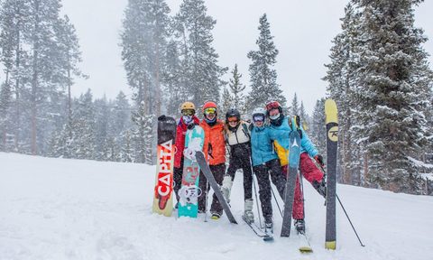 A group of friends posing with their snowboards and skis while standing in the snow.
