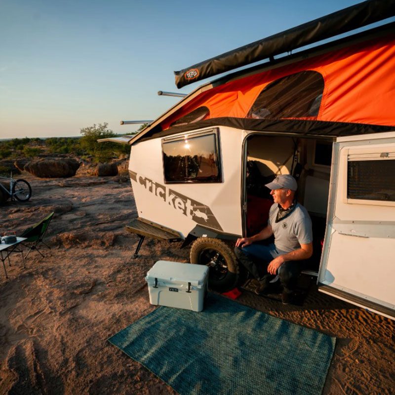 Man camping in a TAXA Outdoors Cricket ultralight travel trailer.