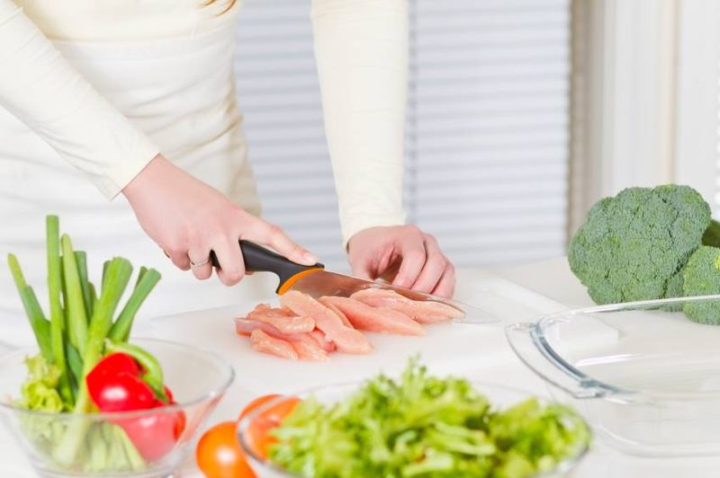 Hands preparing raw chicken and vegetables