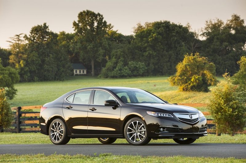 2015 Acura TLX exterior front end angle from passenger side in front of green trees.
