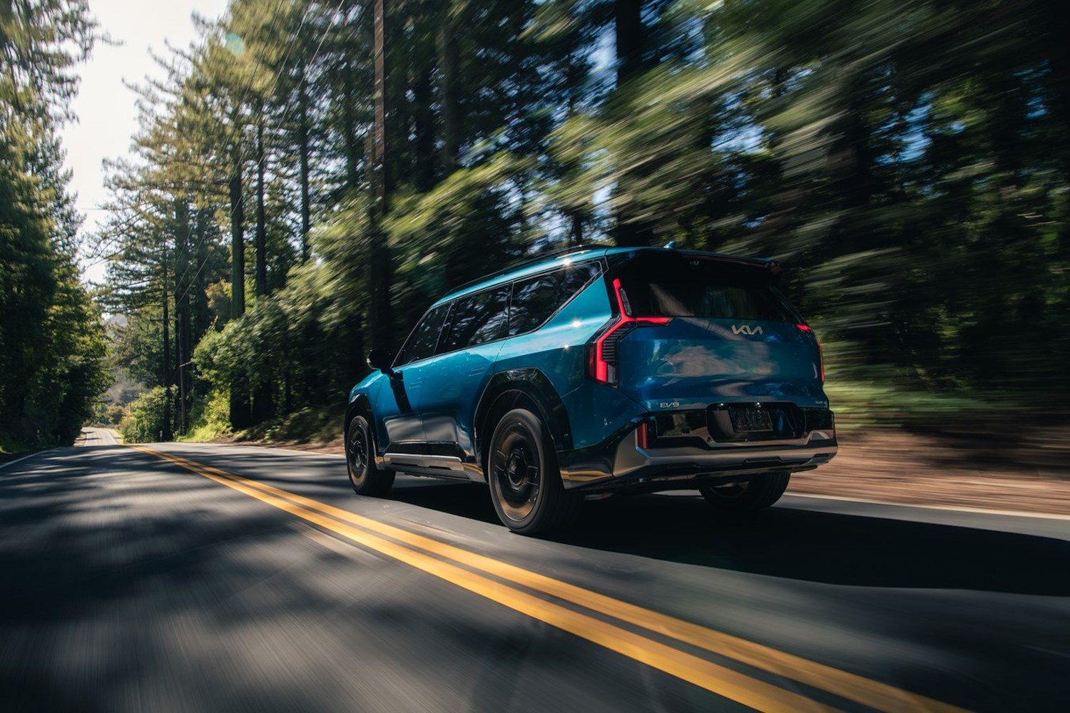 2024 Kia EV9 GT-Line rear end angle driving down the road with mountains in the back.