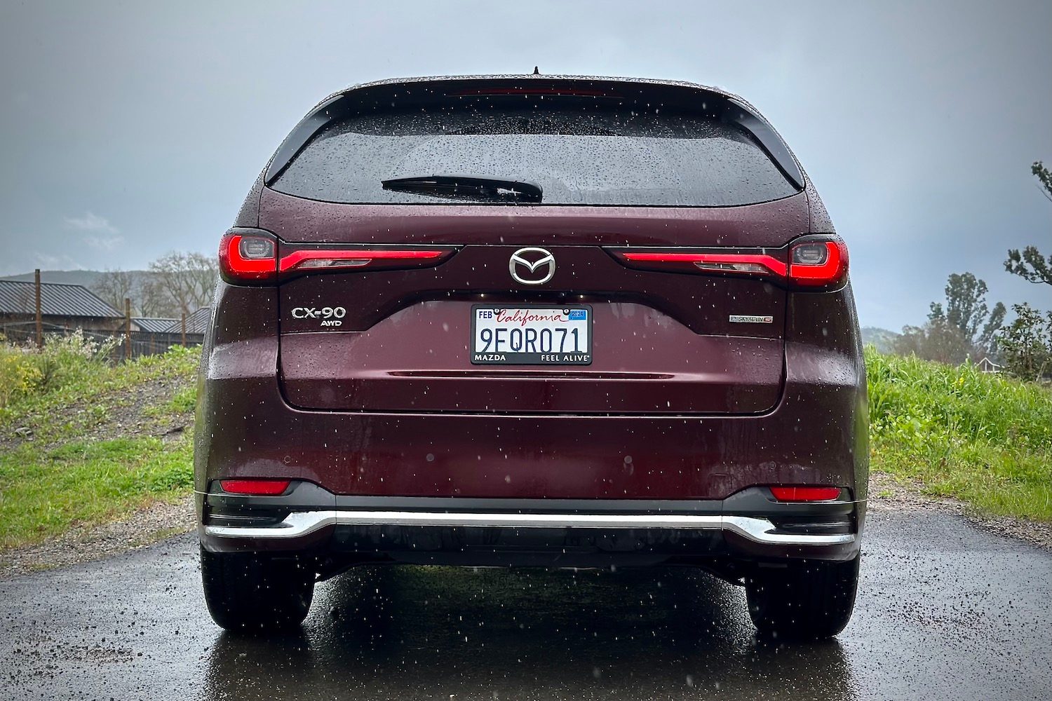 Close up of rear end of the 2024 Mazda CX-90 parked in front of green grass.