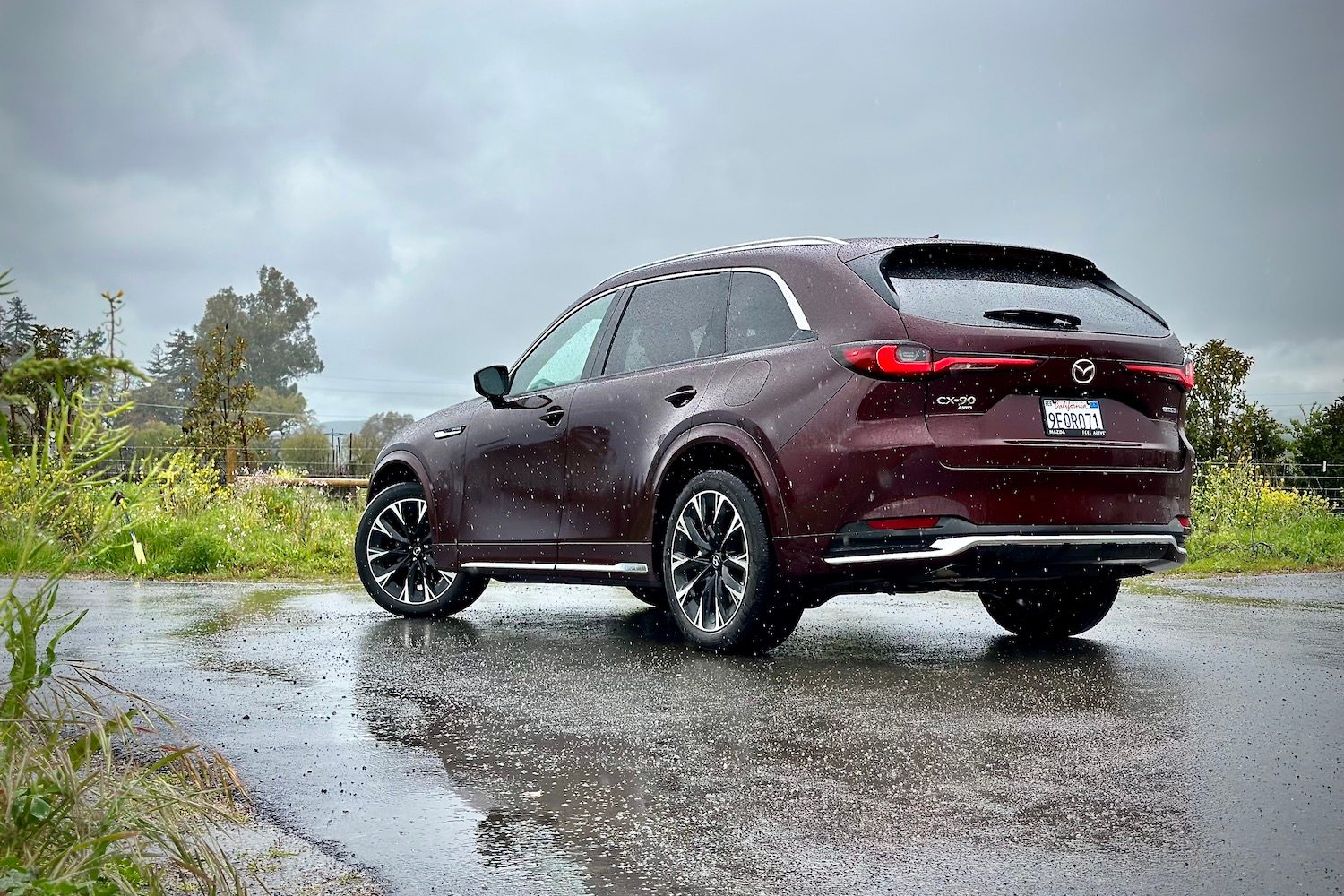 Side profile of the 2024 Mazda CX-90 parked in front of green buses.