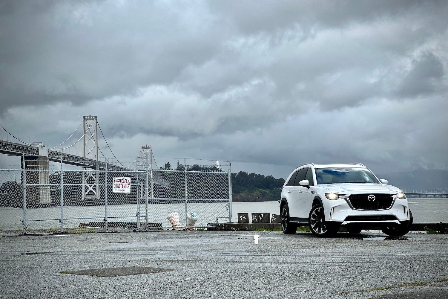 Front end angle of the 2024 Mazda CX-90 PHEV parked in front of a bridge and dark clouds.