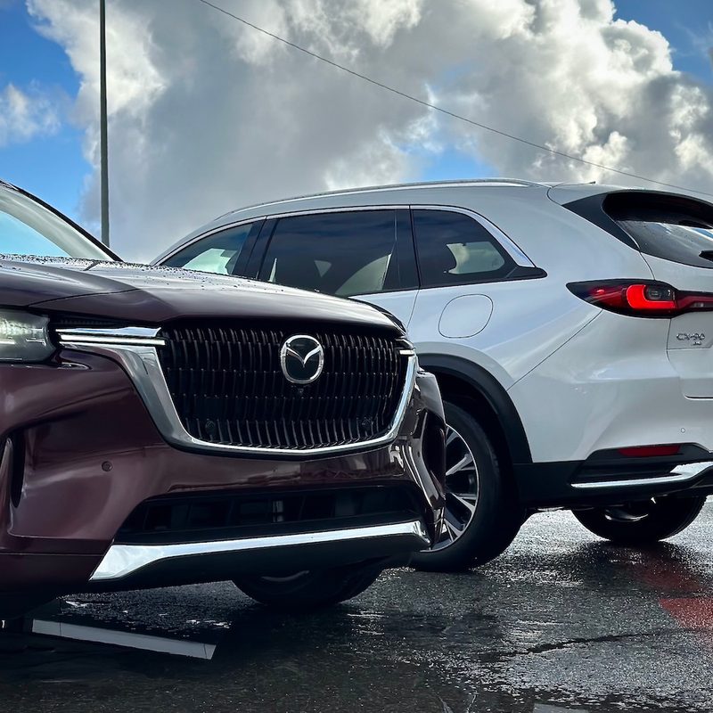 Front and rear end of the 2024 Mazda CX-90 and PHEV parked in front of dark clouds.
