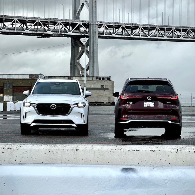 2024 Mazda CX-90 and PHEV parked in front of a large bridge.