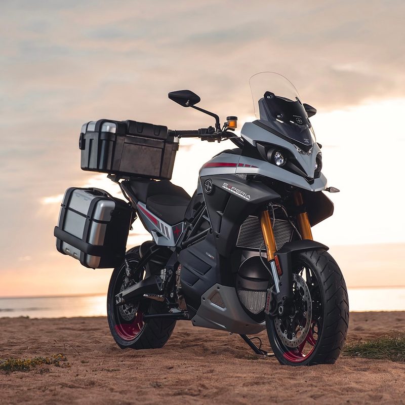 Energica Experia Green Tourer front end angle parked on a beach with a setting sun in the back.