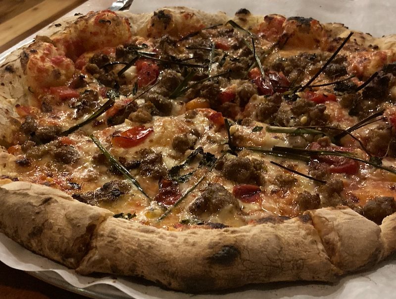 Sausage pizza with roasted peppers, wild spring onions, and herbs.