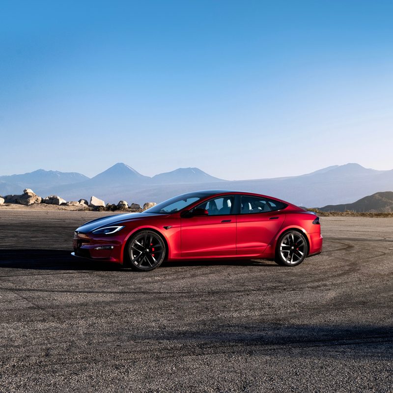 Tesla Model S side profile from front end parked in front of mountains with a blue sky.