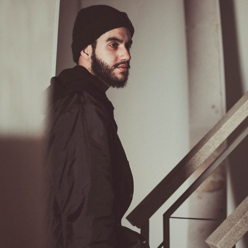 Bearded young man with a skull cap on walking up stairs.
