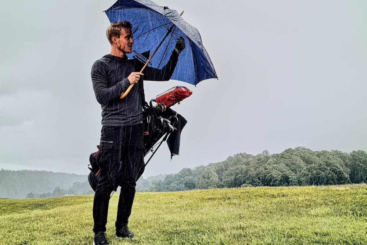man on golf course in rain storm with umbrella