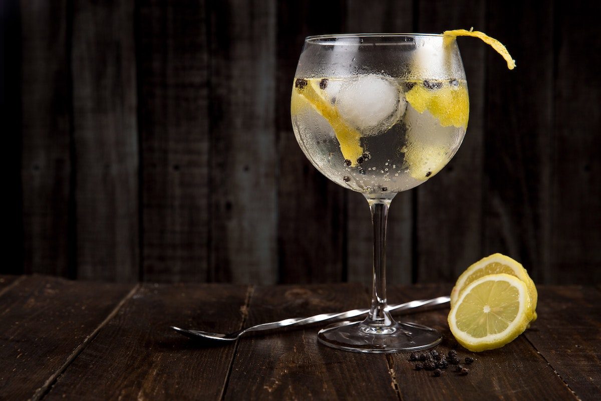 a clear beverage with ice in a glass on dark wooden table